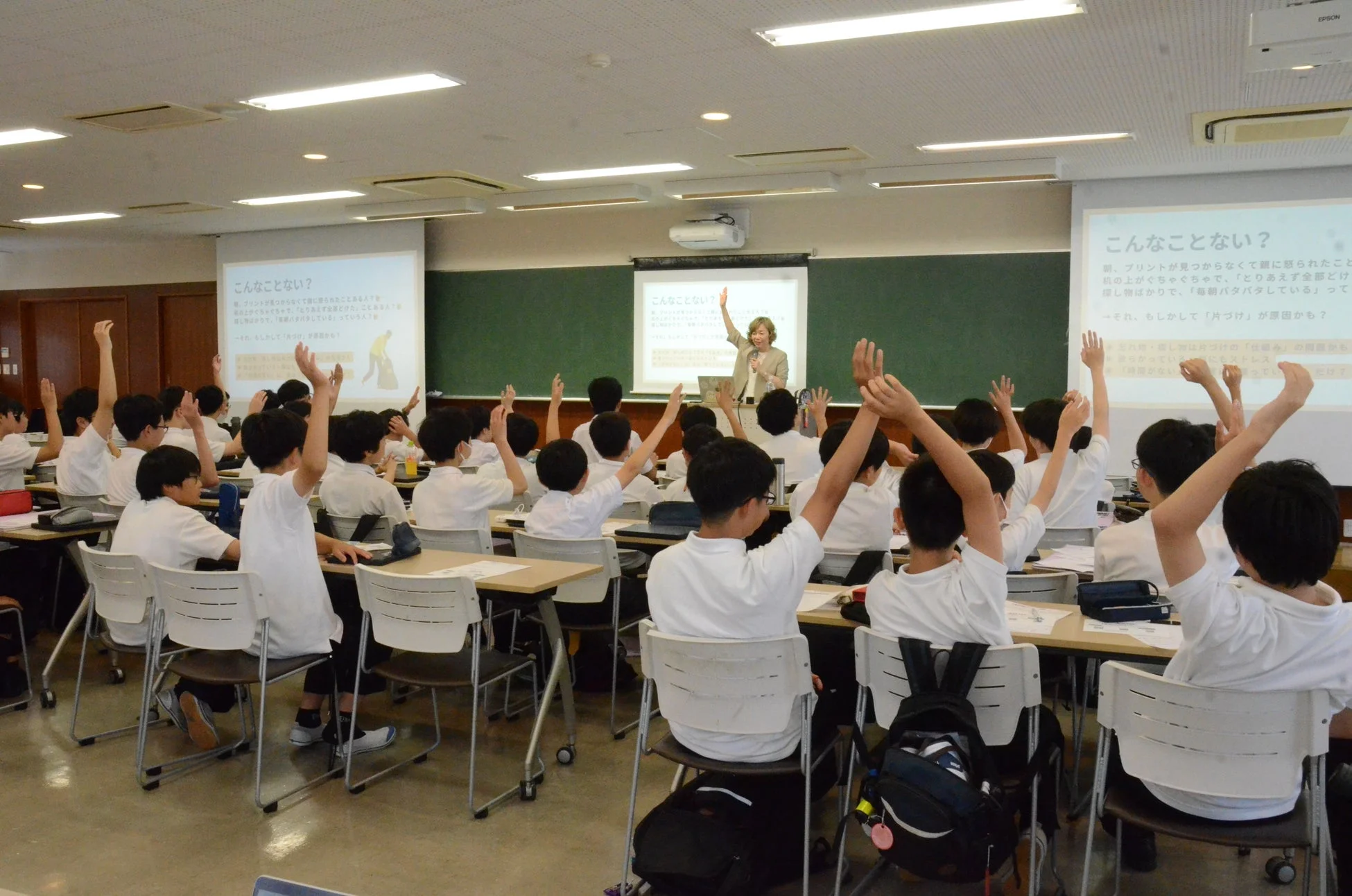 教室で生徒が手を挙げて先生の話を聞いている様子