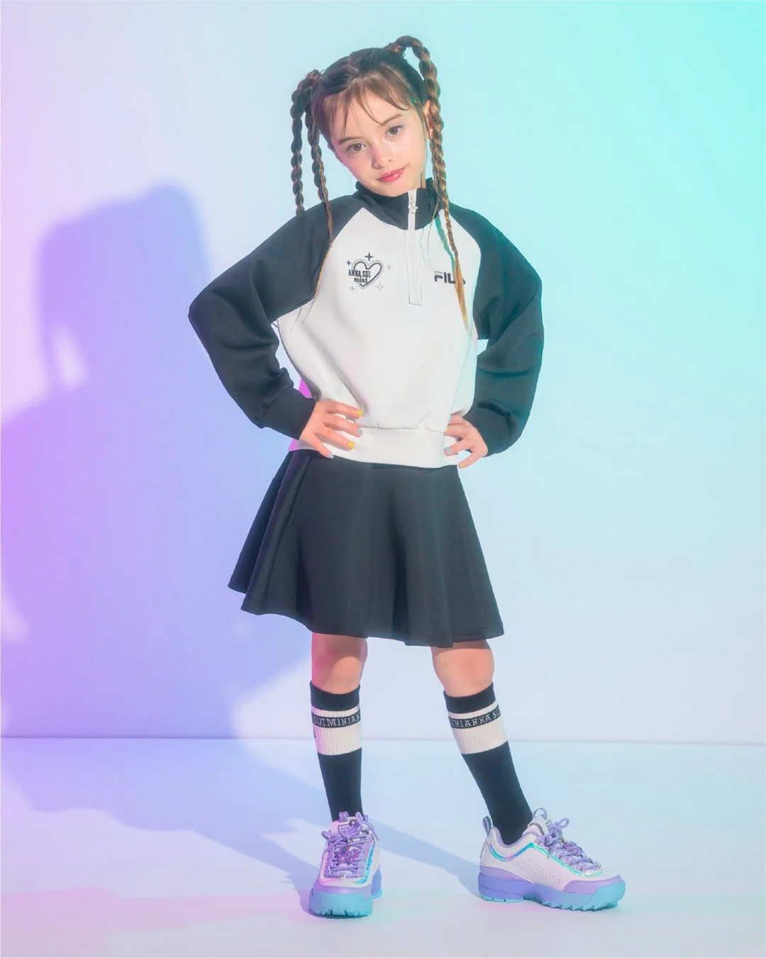 カラフルなスタジオで、ブレイズのツインテールが可愛い女の子の全身ポートレート。黒白のスポーティなスウェットに黒スカート、カラフルなスニーカーを合わせたカジュアルファッションが、元気で魅力的な印象を与えています。