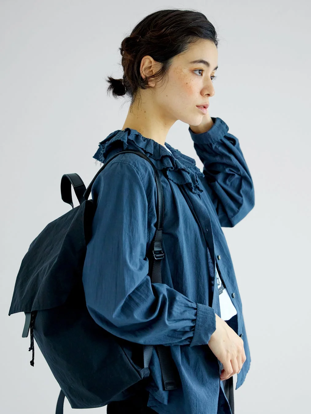青いフリルブラウスを着て黒いリュックを背負った女性の横顔ポートレート