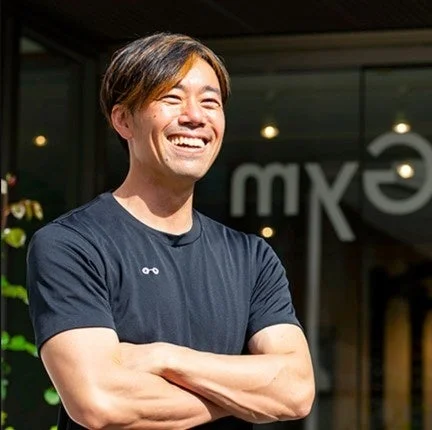 屋外で腕を組み、明るく笑うアジア人男性のポートレートです。
