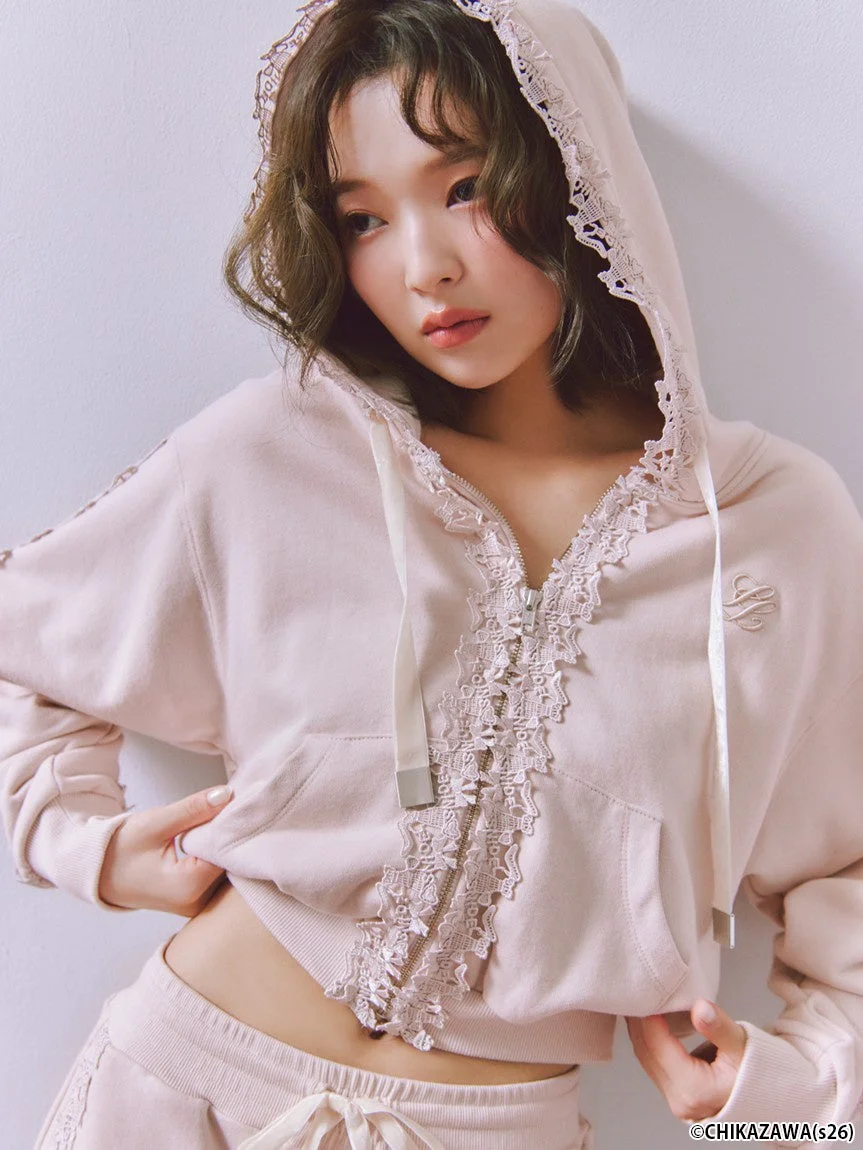 ピンクのレースがあしらわれたショート丈パーカーとボトムスを着用した女性が、カメラを見つめているポートレート。