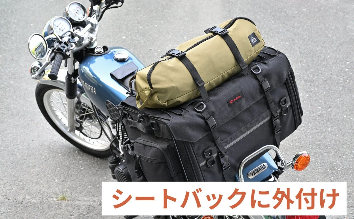青いYAMAHAのバイクのリアシートに、黒い大型のシートバッグとカーキ色のロールバッグがしっかりと固定されている