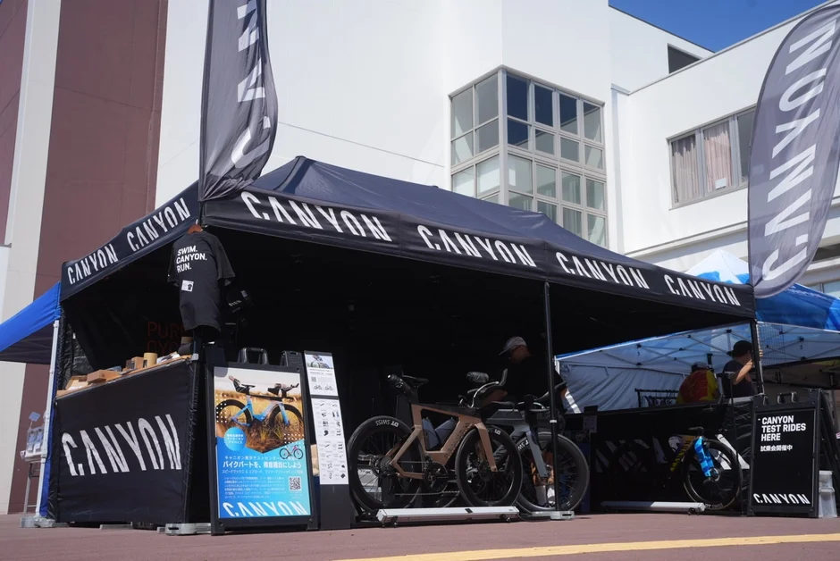 CANYONブランドの自転車試乗会イベントが屋外で開催されている様子です。黒いテントの下には複数のロードバイクが展示され、参加者が試乗できるようになっています。