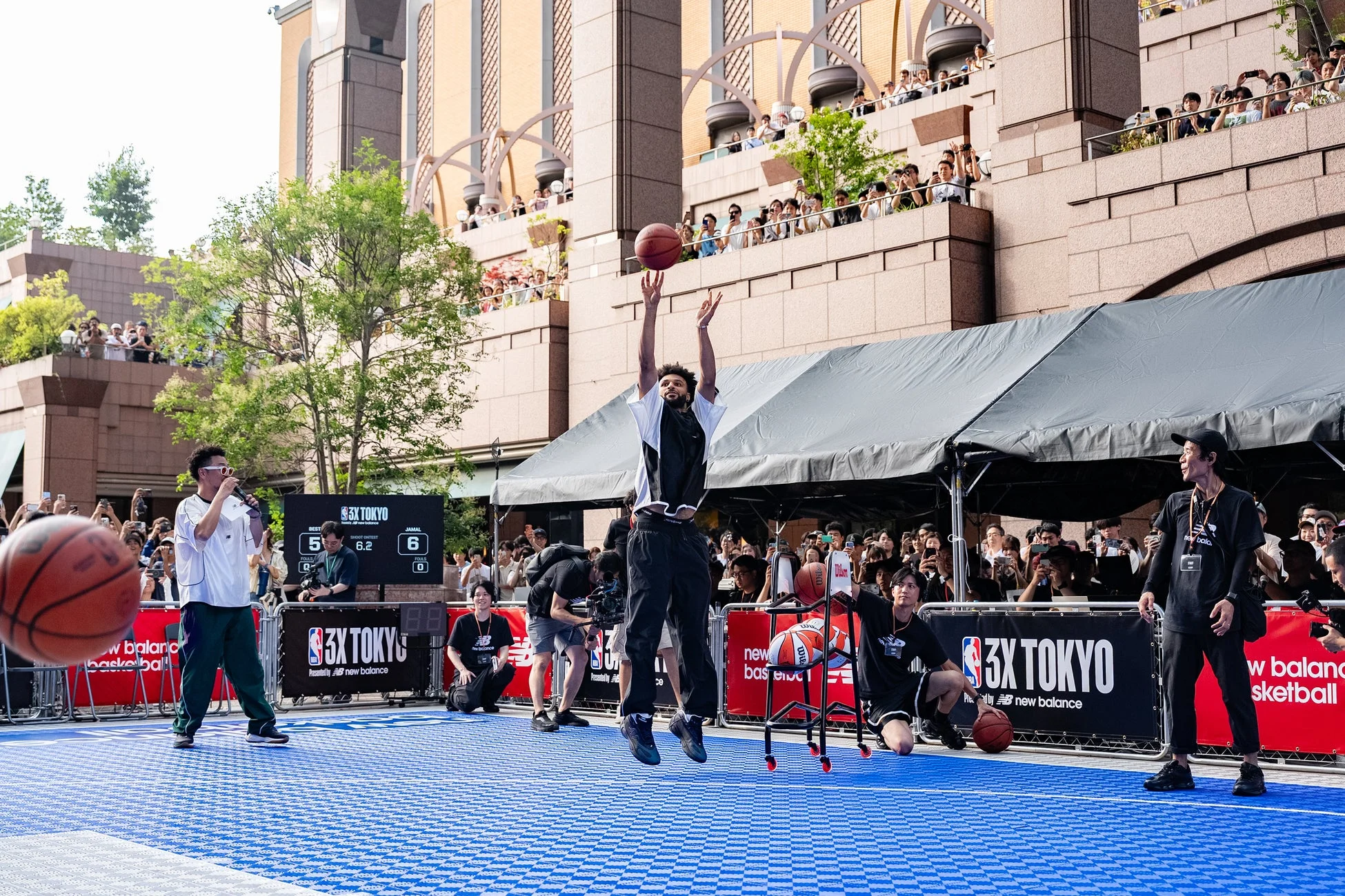 東京の屋外会場で3x3バスケットボールイベントが開催されており、一人の選手がシュートを放っている瞬間です。