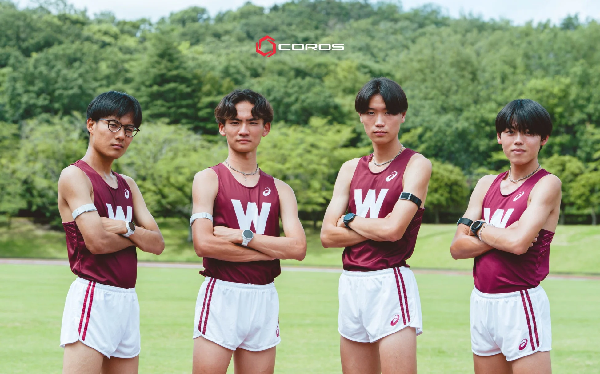 陸上競技のユニフォームを着た4人の若い男性アスリートが、腕を組んでカメラを見つめている。
