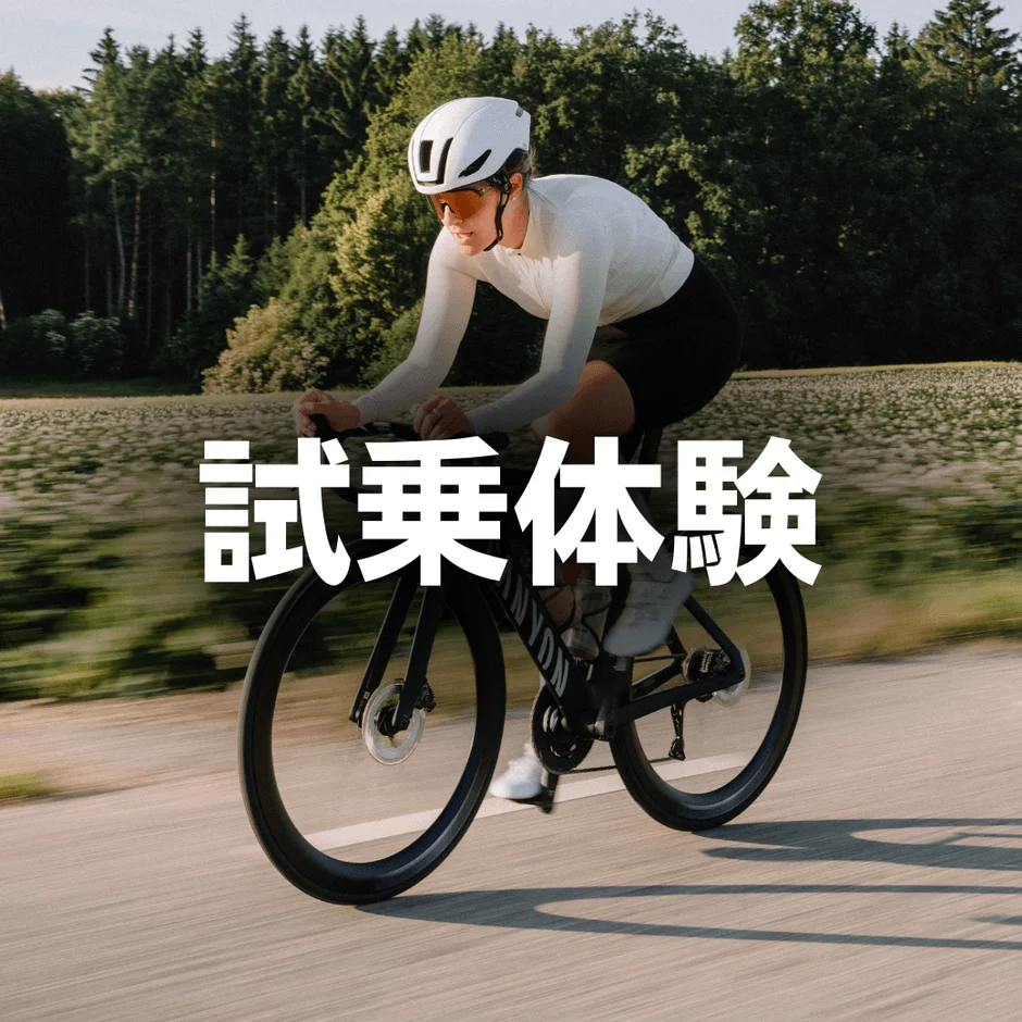 白いヘルメットとサングラスを着用した人がロードバイクに乗って舗装された道を走行しています。