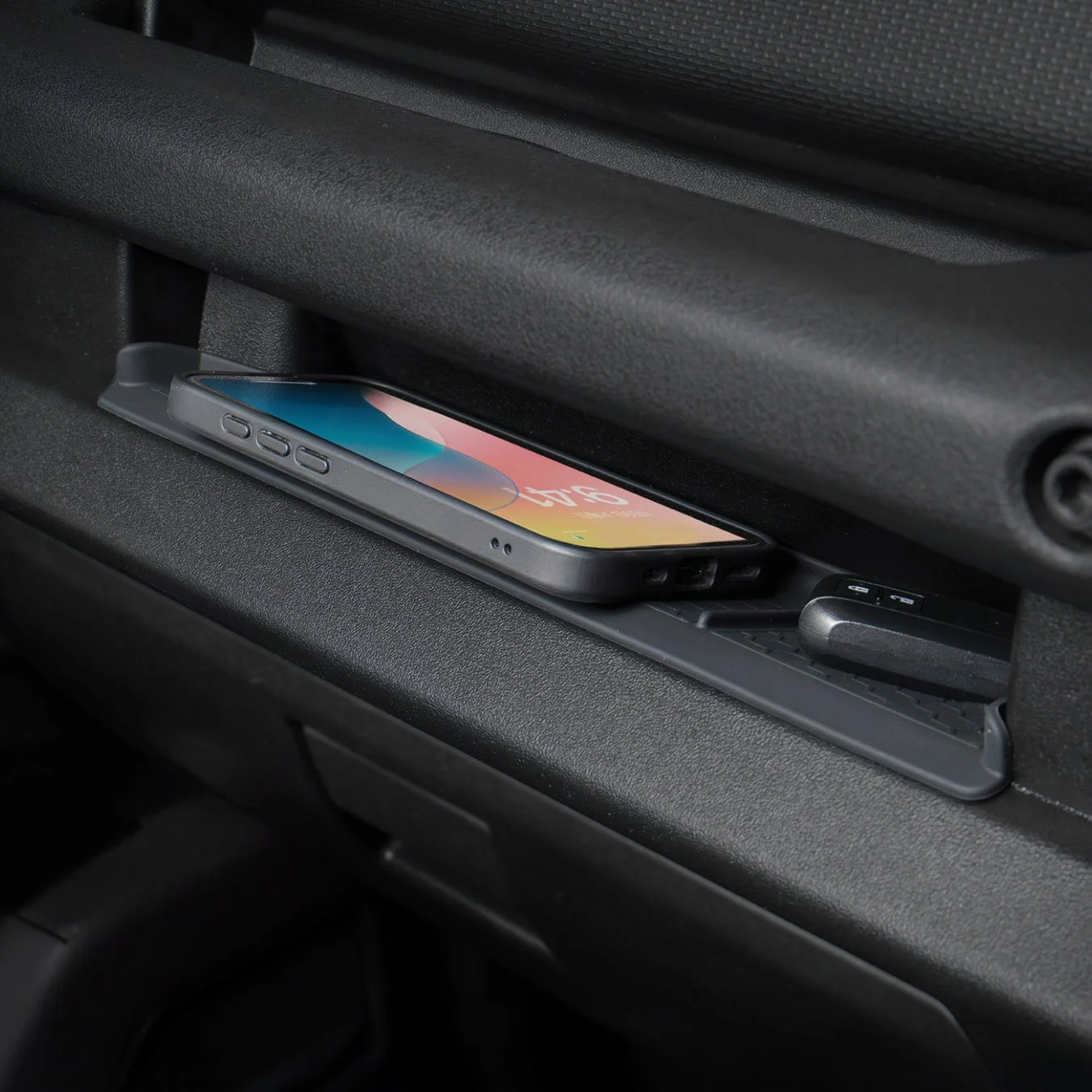 車内の収納スペースに置かれたスマートフォンと車のキーフォブを捉えた画像です。スマートフォンは滑り止めマットの上にあり、画面には時刻「9:47」が表示されています。