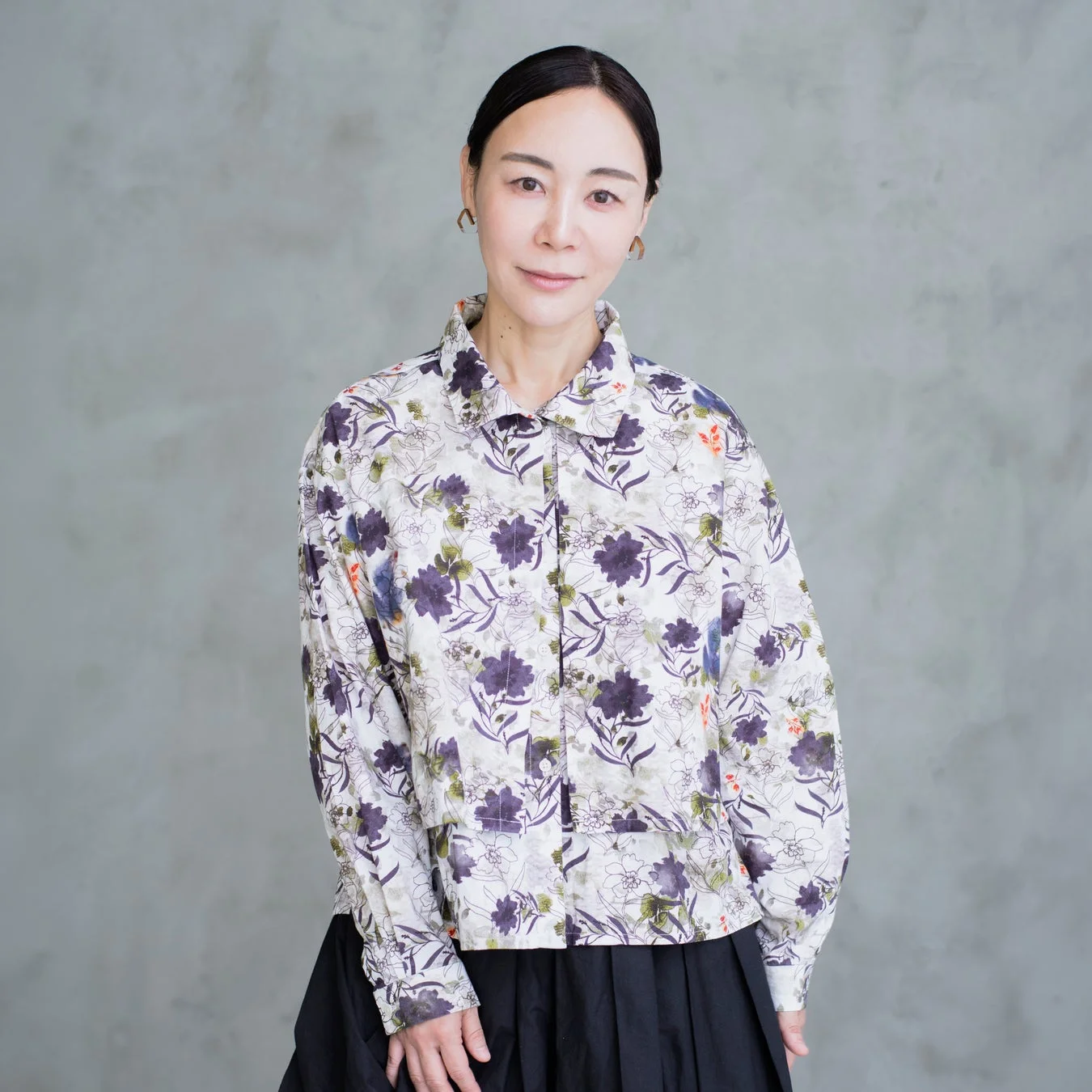 花柄のシャツと黒いプリーツスカートを着用した女性