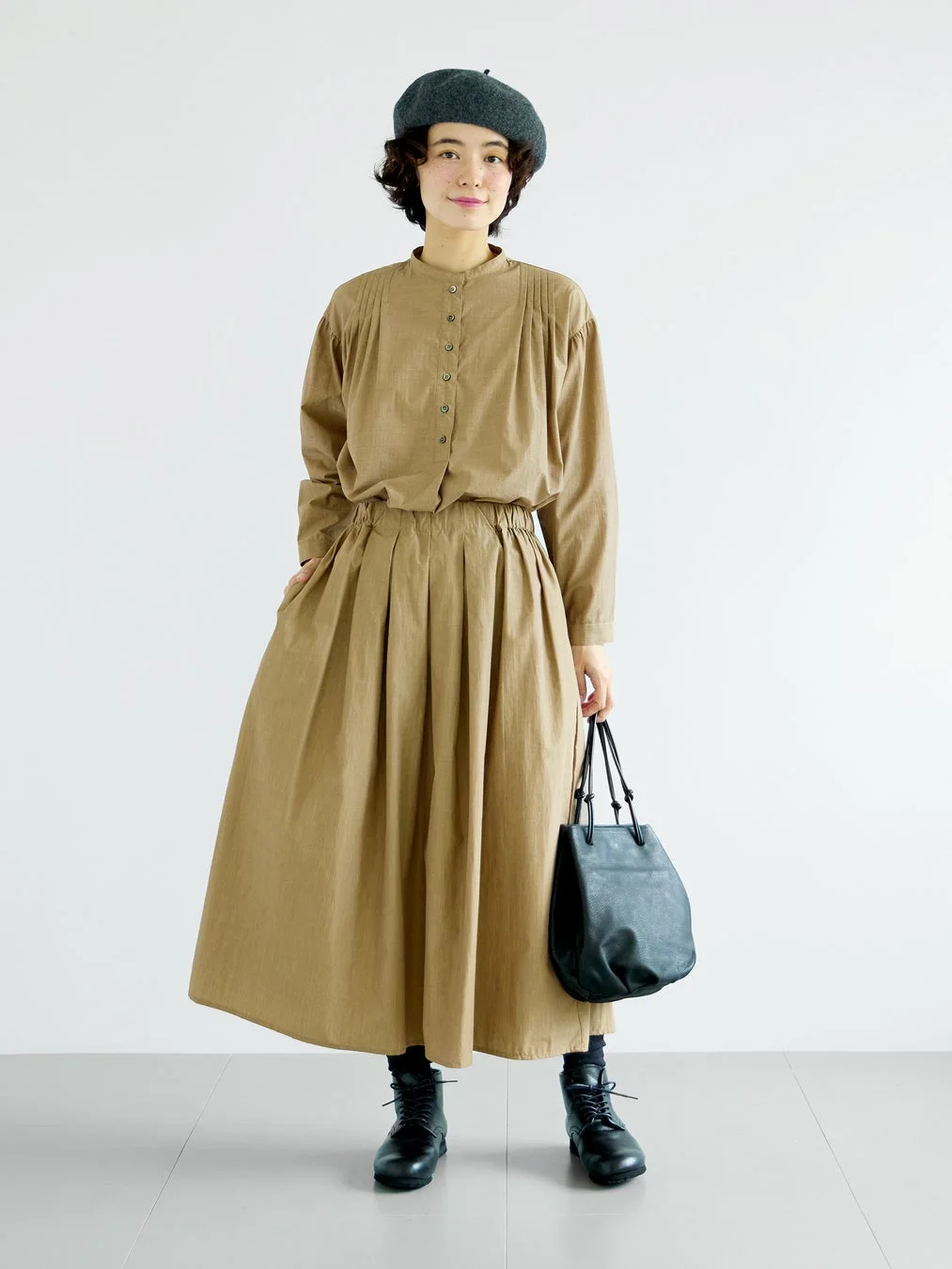 ベージュのスタンドカラーブラウスとプリーツスカートのセットアップを着用した女性