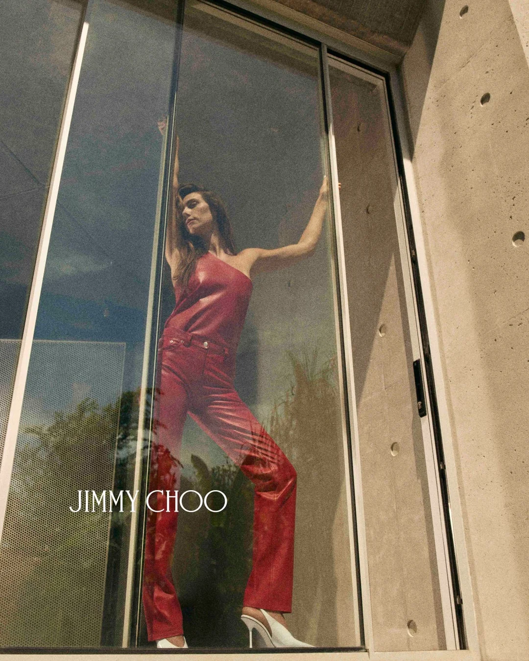 JIMMY CHOOの赤いレザースーツと白いハイヒールを着用した女性