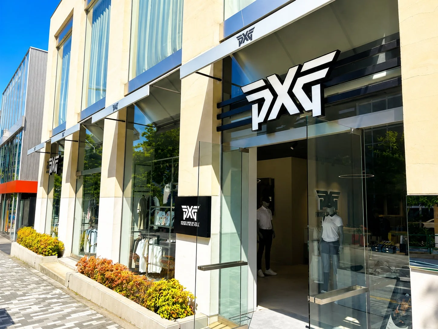 晴れた日に撮影されたPXG店舗の外観。大きなロゴが特徴的で、ガラス張りのショーウィンドウにはアパレルが展示されています。店頭には植え込みがあり、モダンな雰囲気が漂っています。