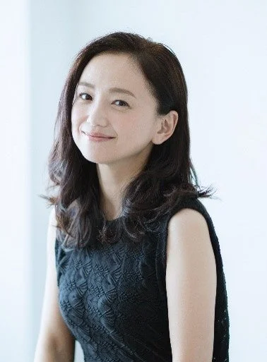黒いノースリーブのトップスを着たアジア人女性が、カメラに向かって優しく微笑んでいます